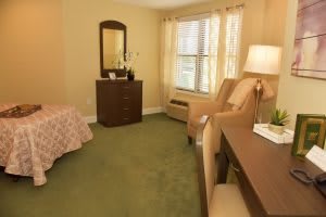 Cozy bedroom interior with a bed, dresser, chairs, and natural light from the window.