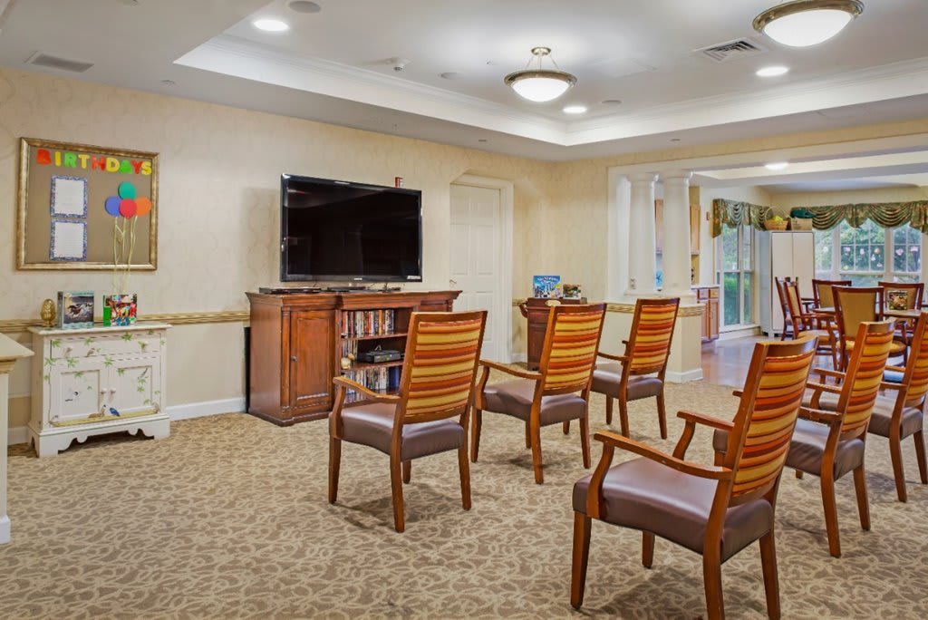 A communal seating area with several wooden chairs facing a television in a cozy room.