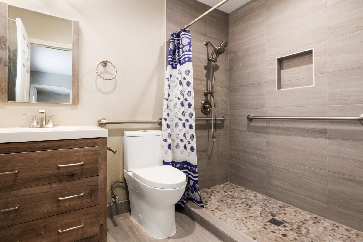 A modern bathroom with a walk-in shower, toilet, and wooden vanity.