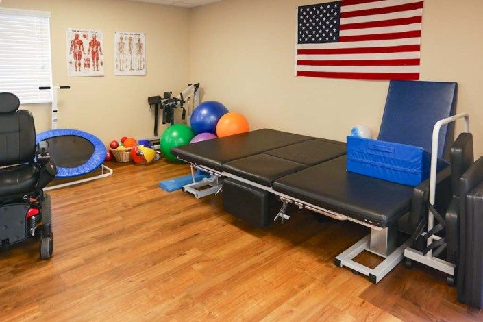 A physical therapy room equipped with exercise balls, a trampoline, and a therapy bed, decorated with an American flag on the wall.