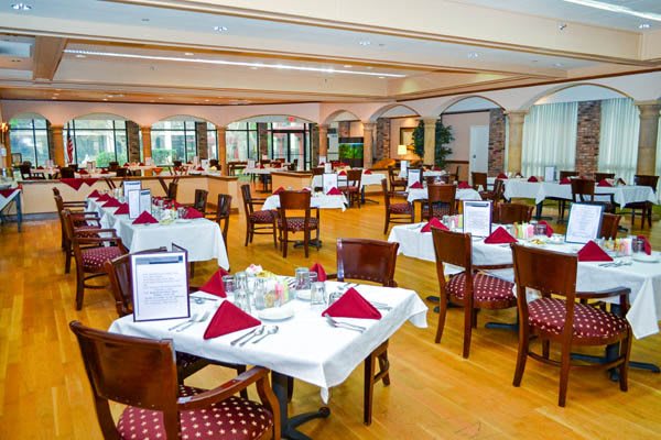 An elegantly set restaurant dining room with tables covered in white tablecloths and arranged neatly.