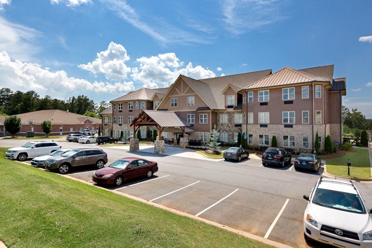 A residential building with a parking lot and several cars under a blue sky with scattered clouds.