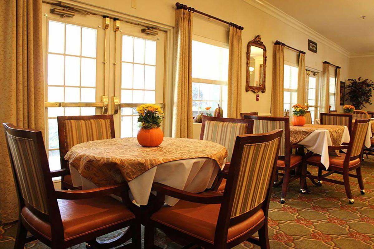 A cozy dining area with elegantly set tables and comfortable chairs, illuminated by natural light from the large windows.