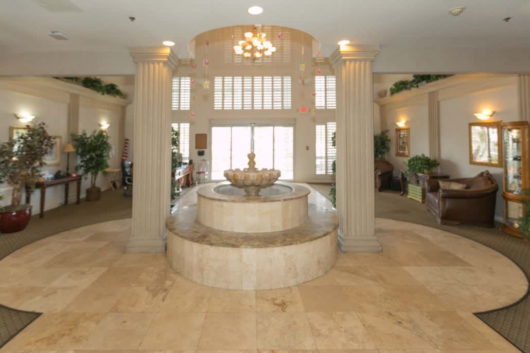 A luxurious lobby featuring a central marble fountain, grand columns, and a chandelier.