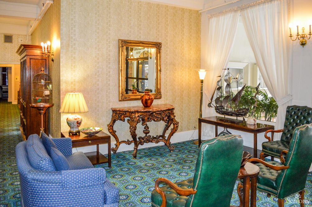 A vintage-style living room featuring ornate furniture, a decorative mirror, and a ship model.