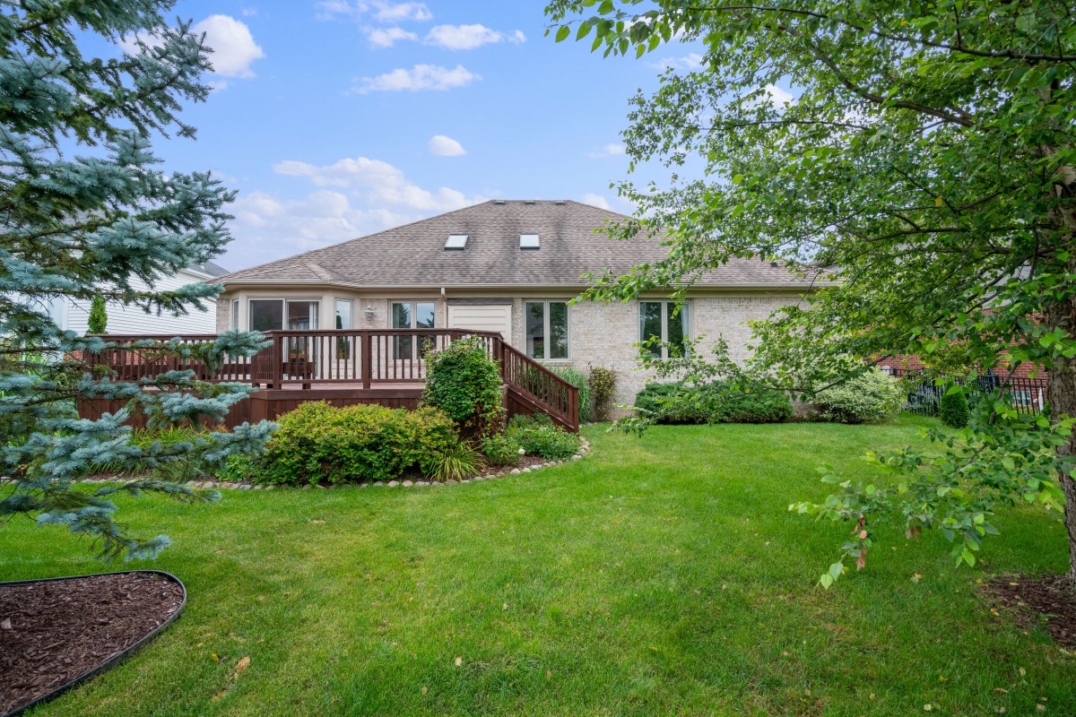 A residential house with a spacious backyard featuring a green lawn and a wooden deck.