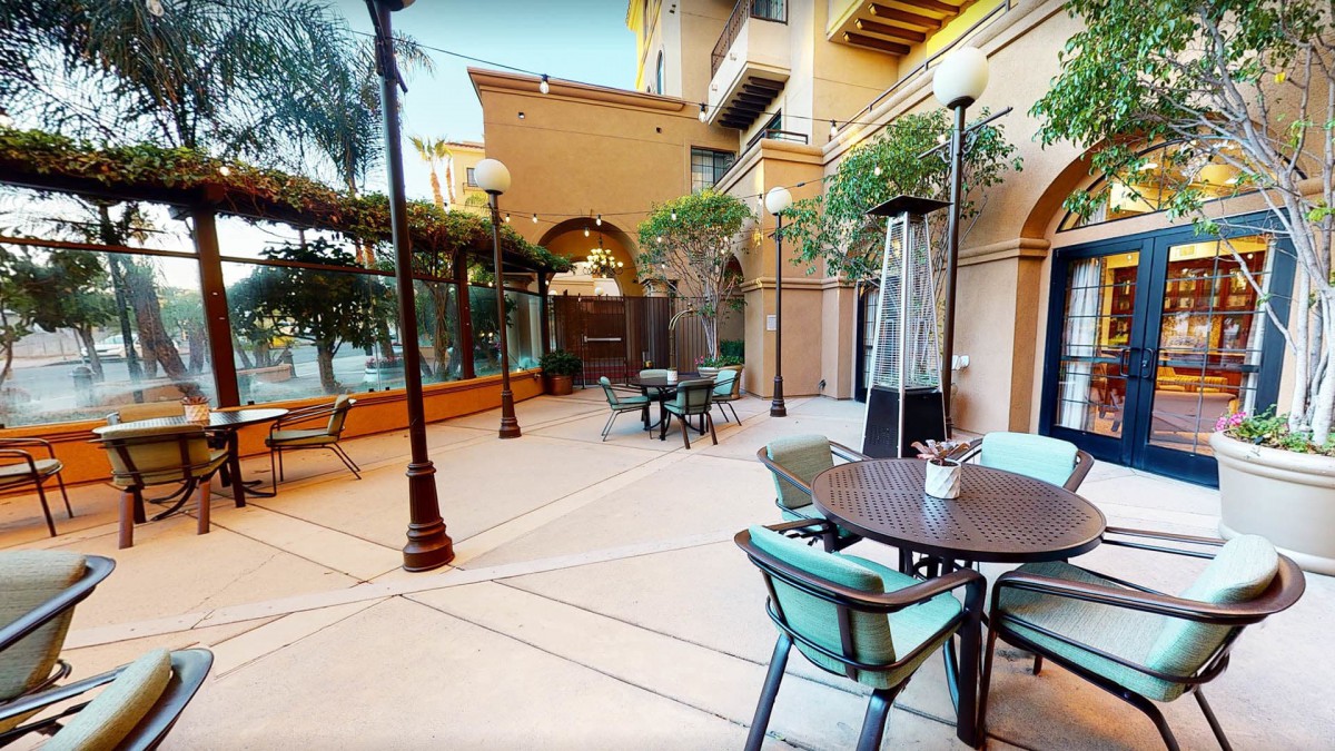 A cozy outdoor patio area with tables, chairs, and surrounding plants.