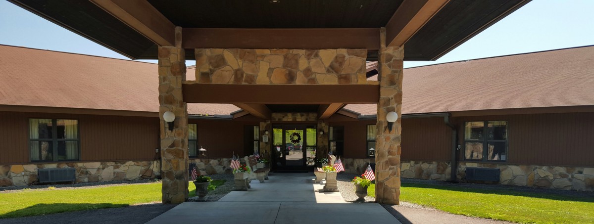 A building entrance with a stone facade, featuring a covered walkway adorned with plants and flags.