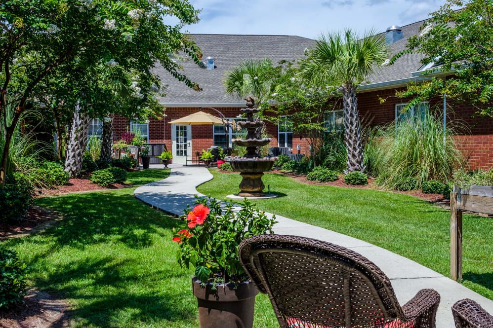 A serene garden with a fountain, lush greenery, and outdoor seating.
