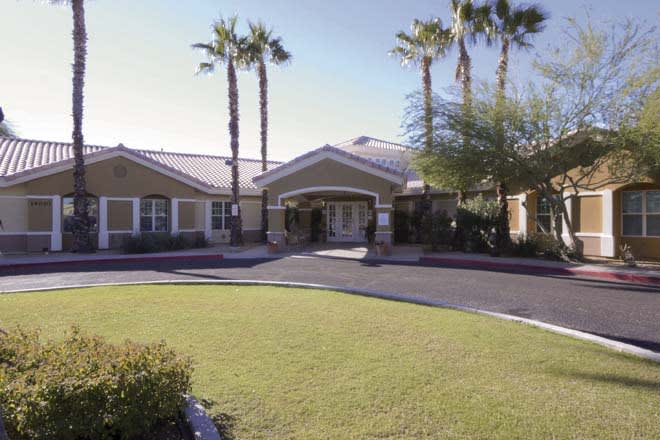 A residential building with a landscaped front yard and palm trees lining the driveway.