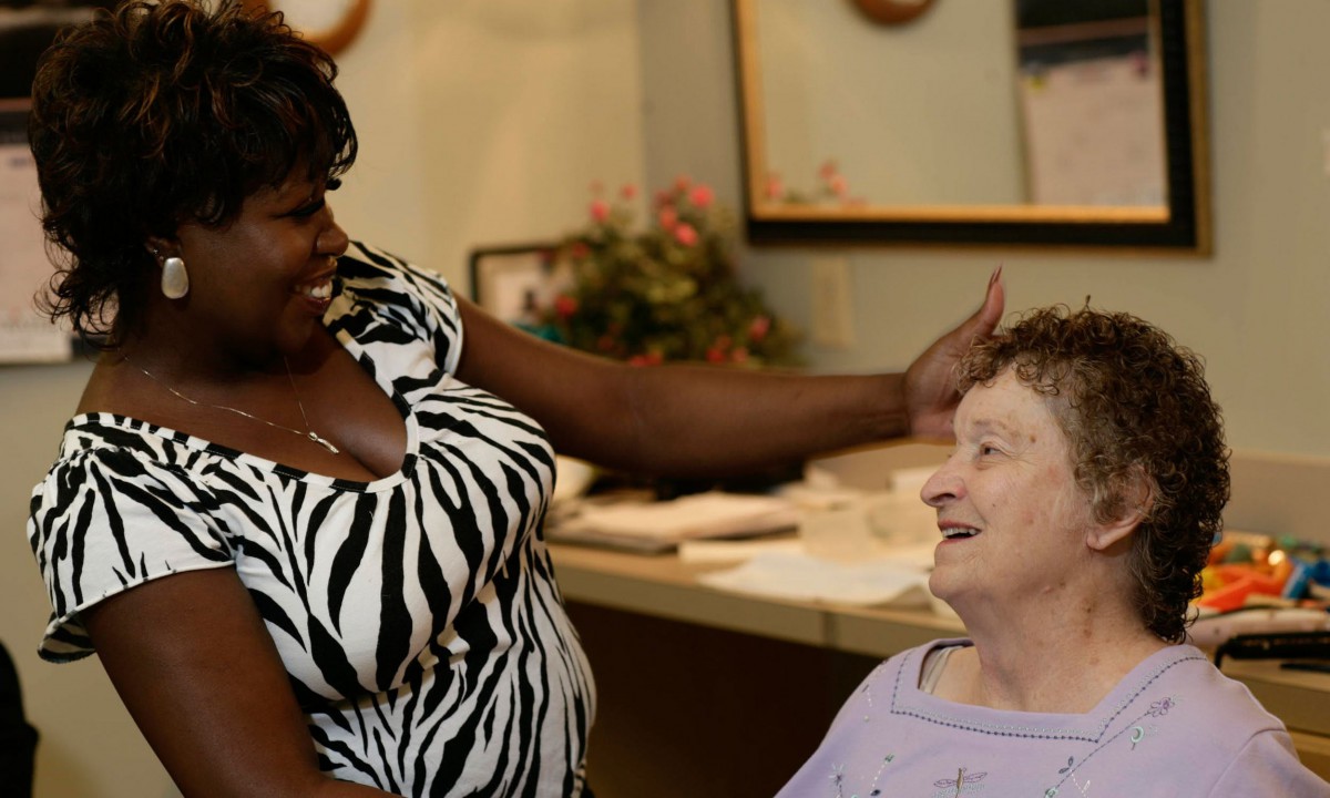 A caregiver interacts warmly with an elderly woman, sharing a moment of joy.
