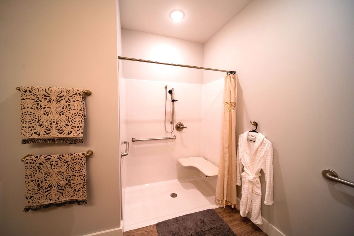 A modern bathroom with an accessible shower featuring a grab bar and foldable seat, complemented by a nearby towel rack and robe.