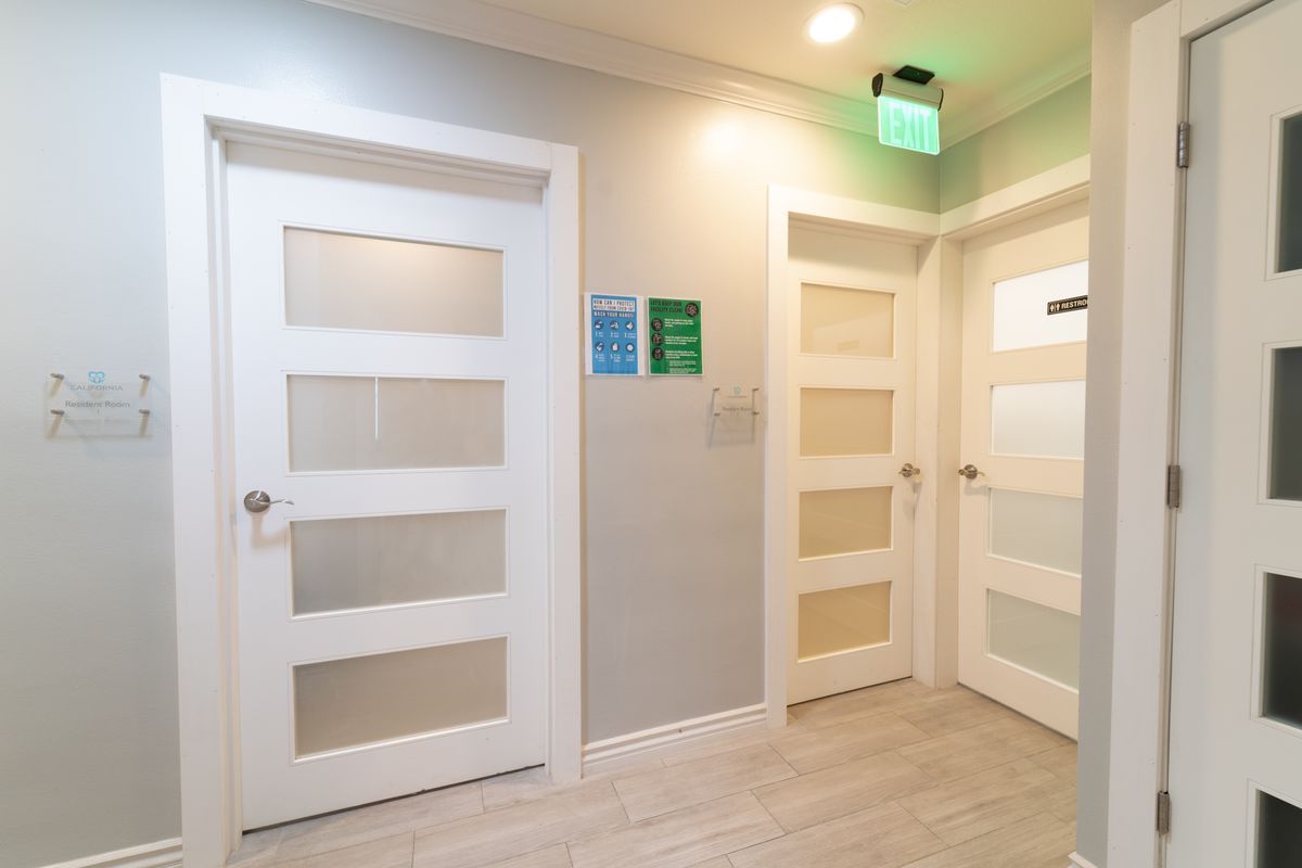 A modern hallway with white doors and an illuminated exit sign.