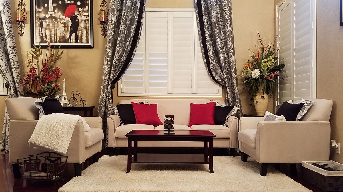 A cozy living room with beige sofas adorned with red and black pillows, complemented by elegant curtains and a central coffee table.