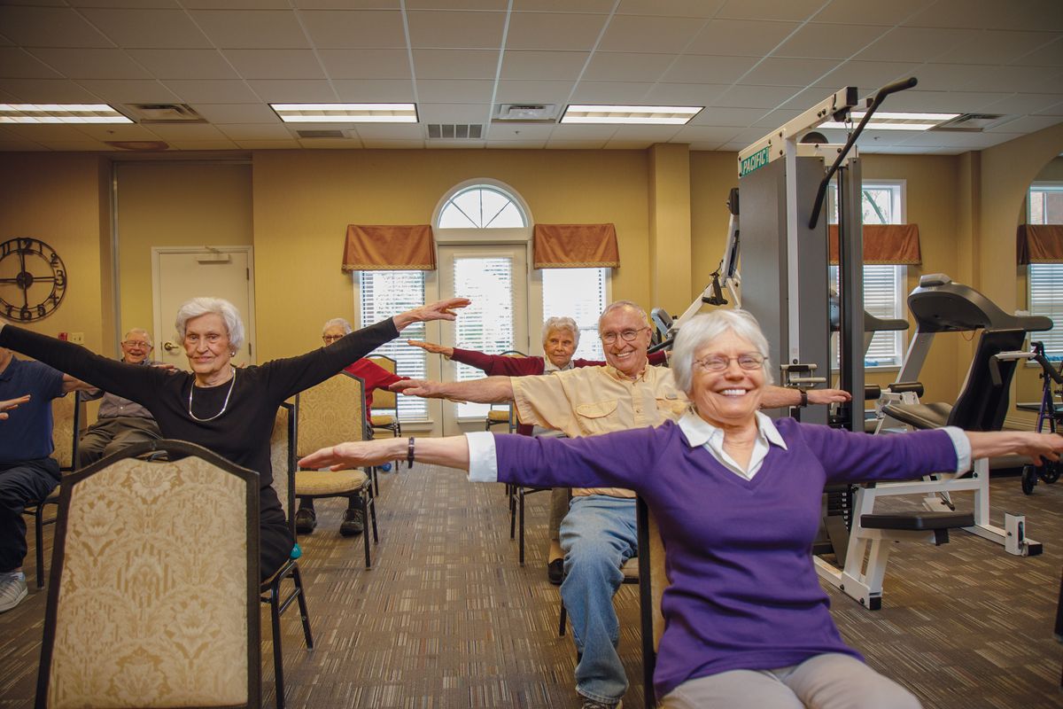 A group of seniors participating in a fitness class indoors, engaging in arm exercises.
