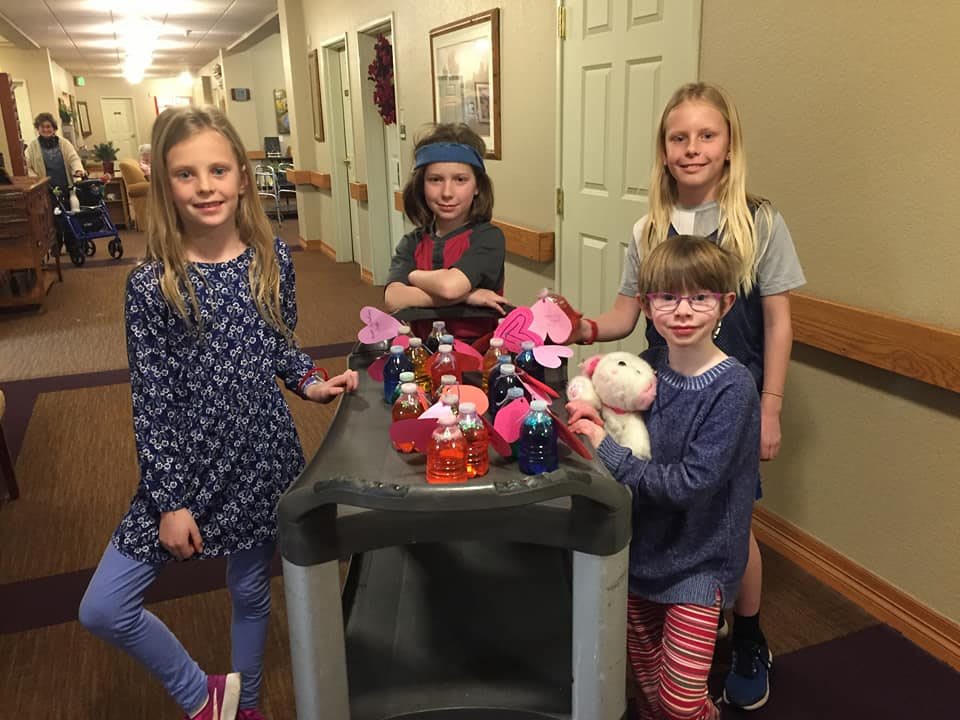 A group of children in a hallway with a cart full of toys.