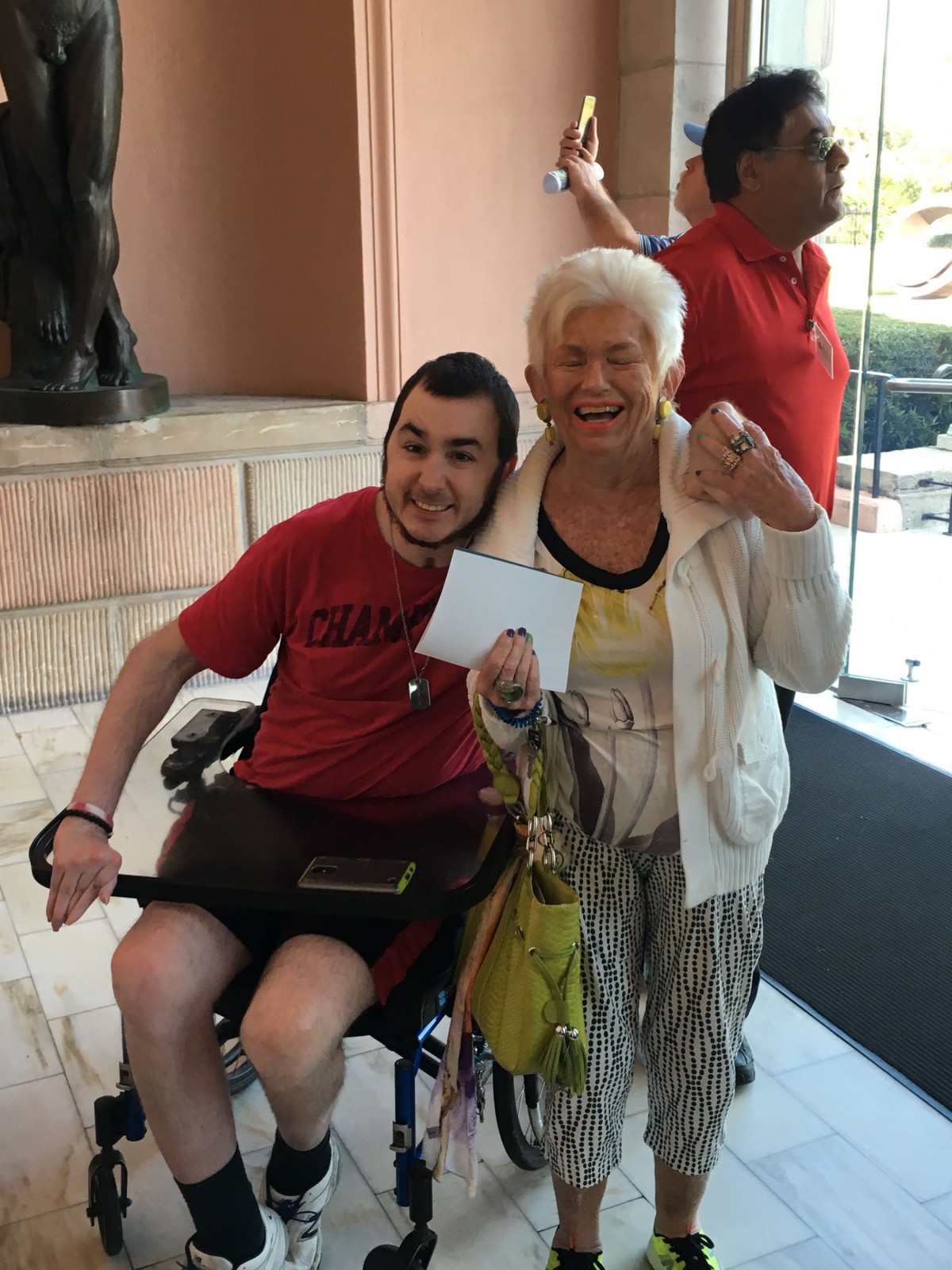 An elderly woman and a young man in a wheelchair share a joyful moment indoors.