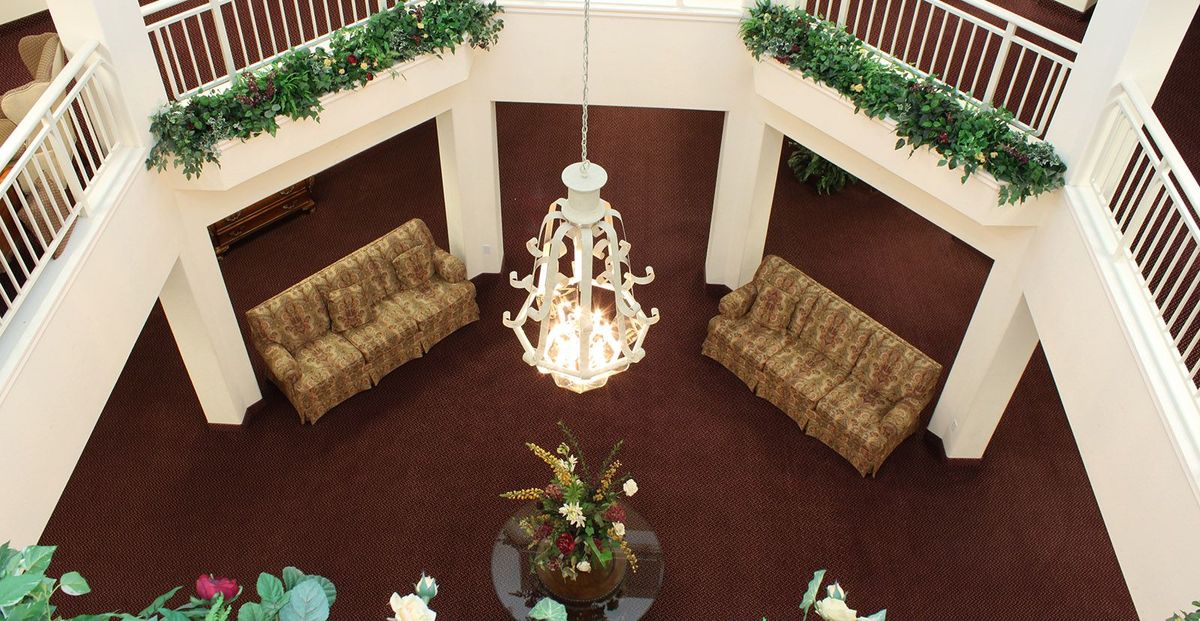 A spacious lobby with a central chandelier, surrounded by sofas and greenery.