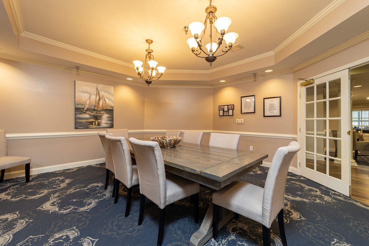 A well-appointed dining room featuring an elegant table, upholstered chairs, two chandeliers, and artwork on the walls.