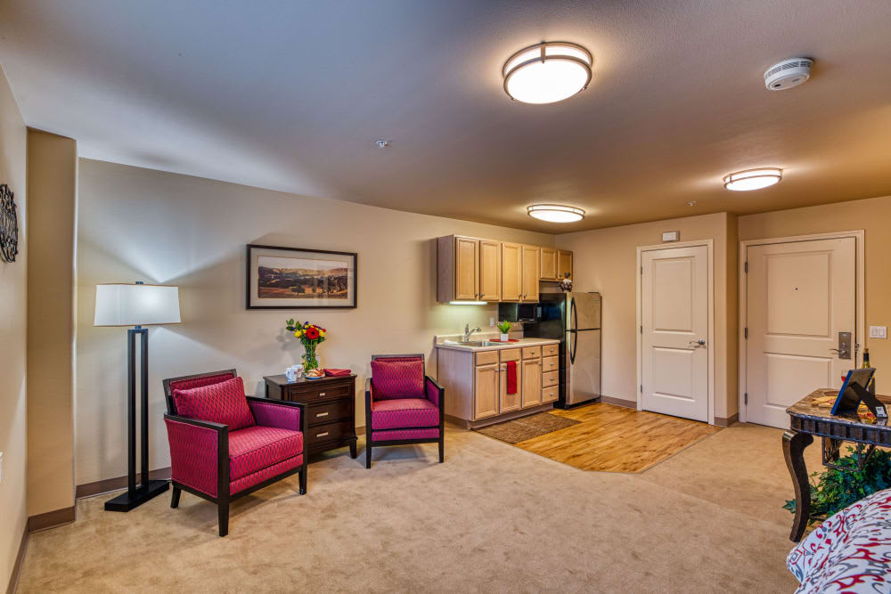 A cozy living space featuring a small kitchen and seating area with vibrant pink chairs.
