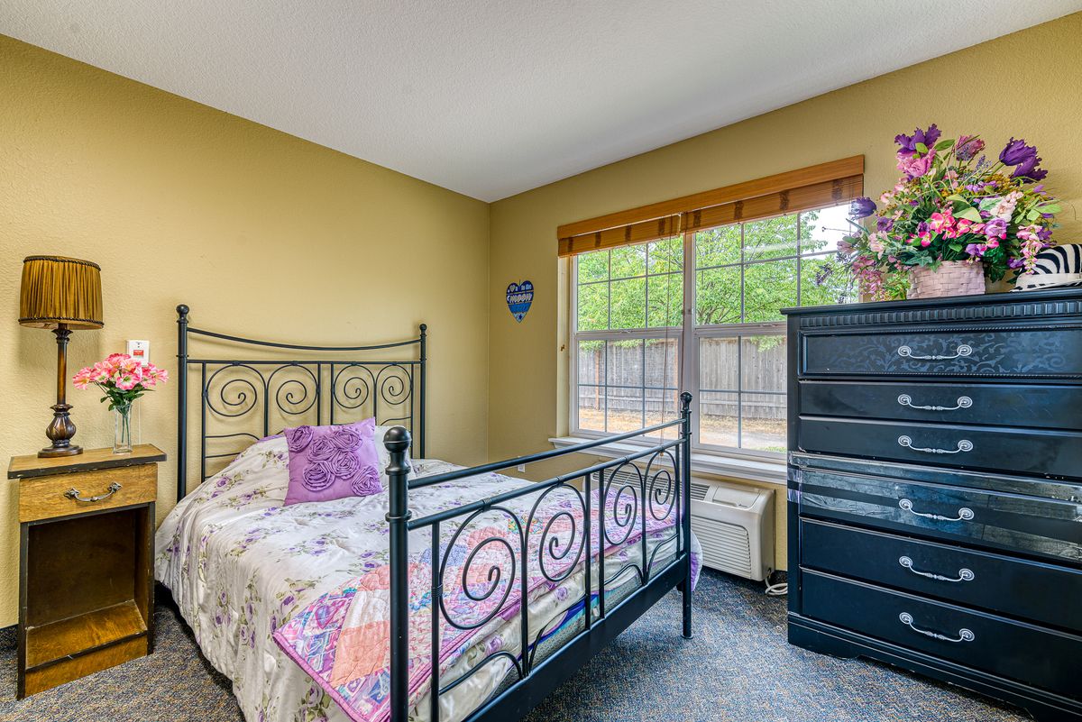 A cozy bedroom with a black metal bed frame, yellow walls, and ample natural light from a large window.