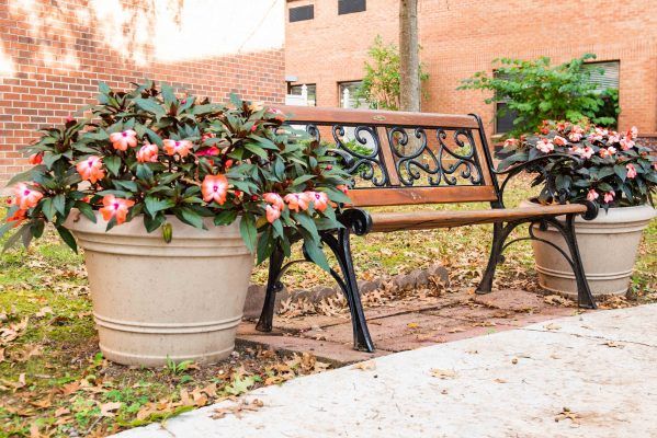 A quaint park bench adorned with potted flowers, set against a brick wall and sidewalk.