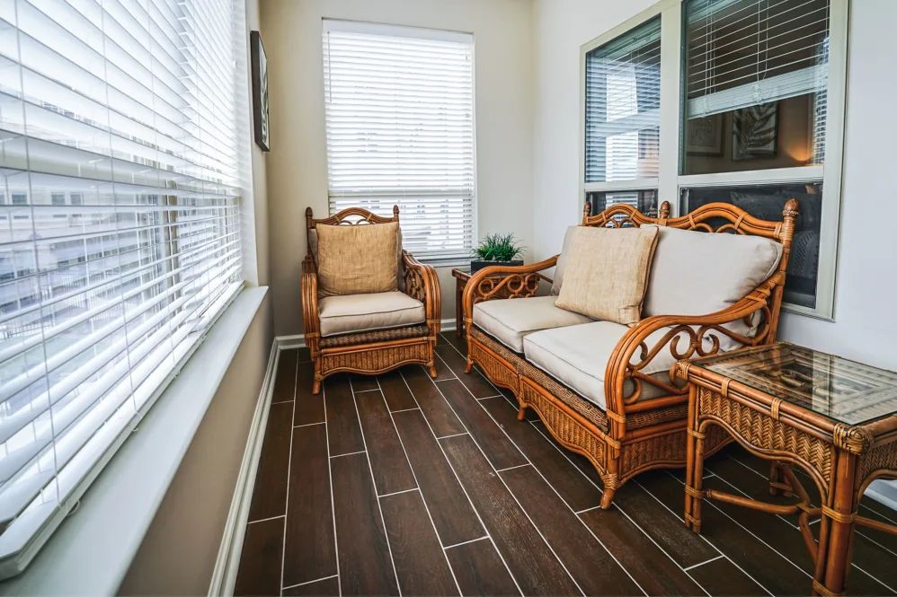 A cozy sunroom with rattan furniture and large windows.