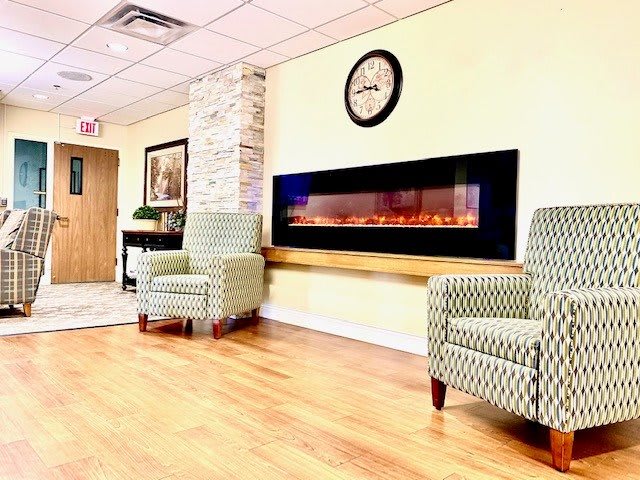 A cozy waiting area featuring comfortable armchairs and an electric fireplace.