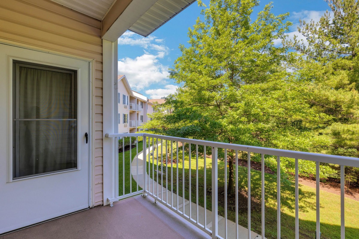 A sunny balcony with a view of greenery and nearby apartments.
