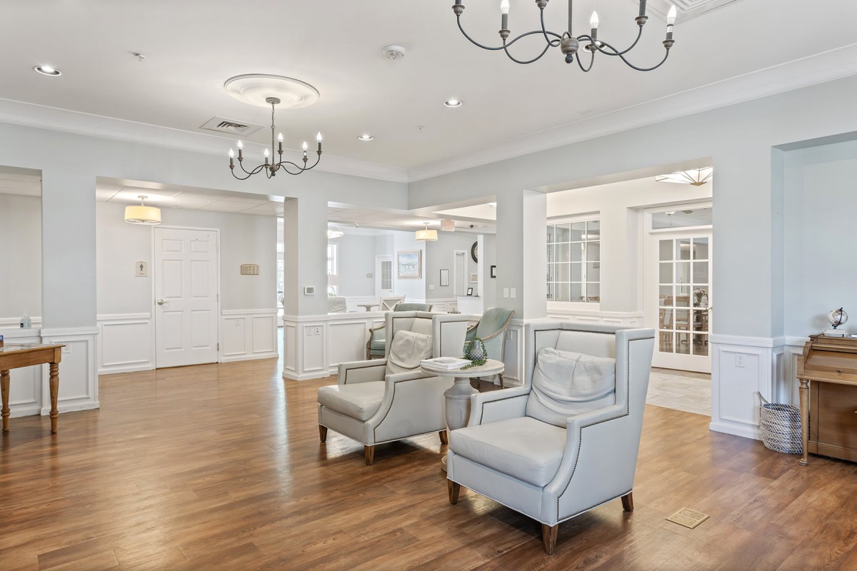 A spacious and elegantly designed living room featuring modern furniture, hardwood flooring, and bright lighting from chandeliers.