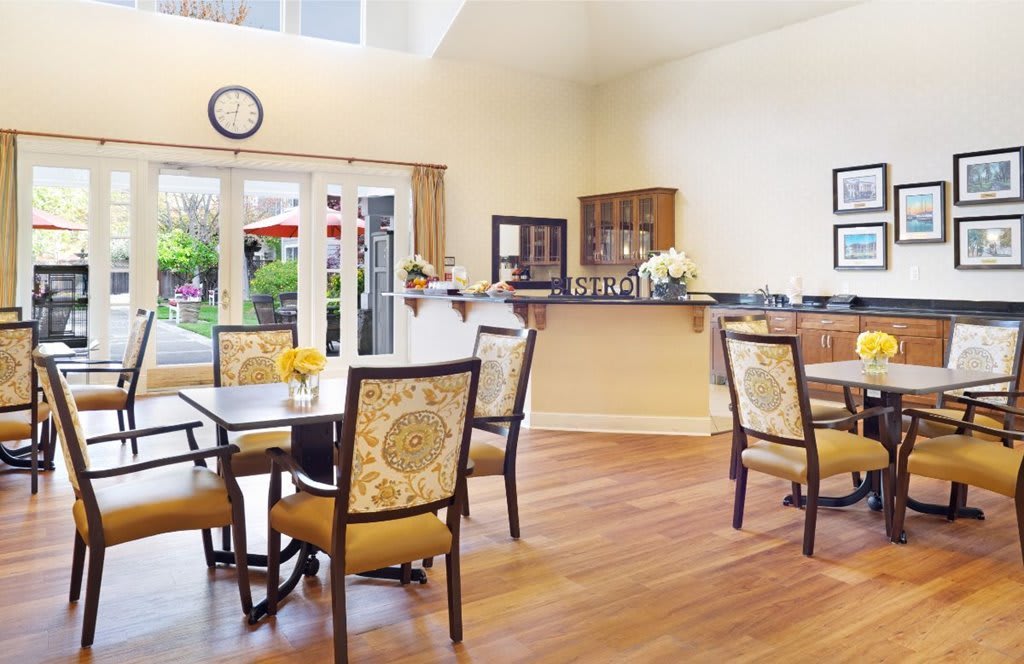 A bright and spacious dining room with wooden floors and elegant furniture, featuring large windows that allow natural light to flood in.