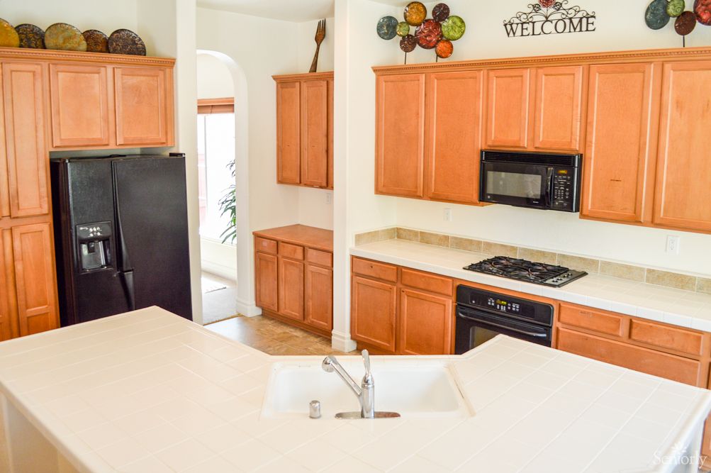 A bright kitchen featuring wooden cabinets, a countertop with a sink, and various appliances including a stove, microwave, and refrigerator.