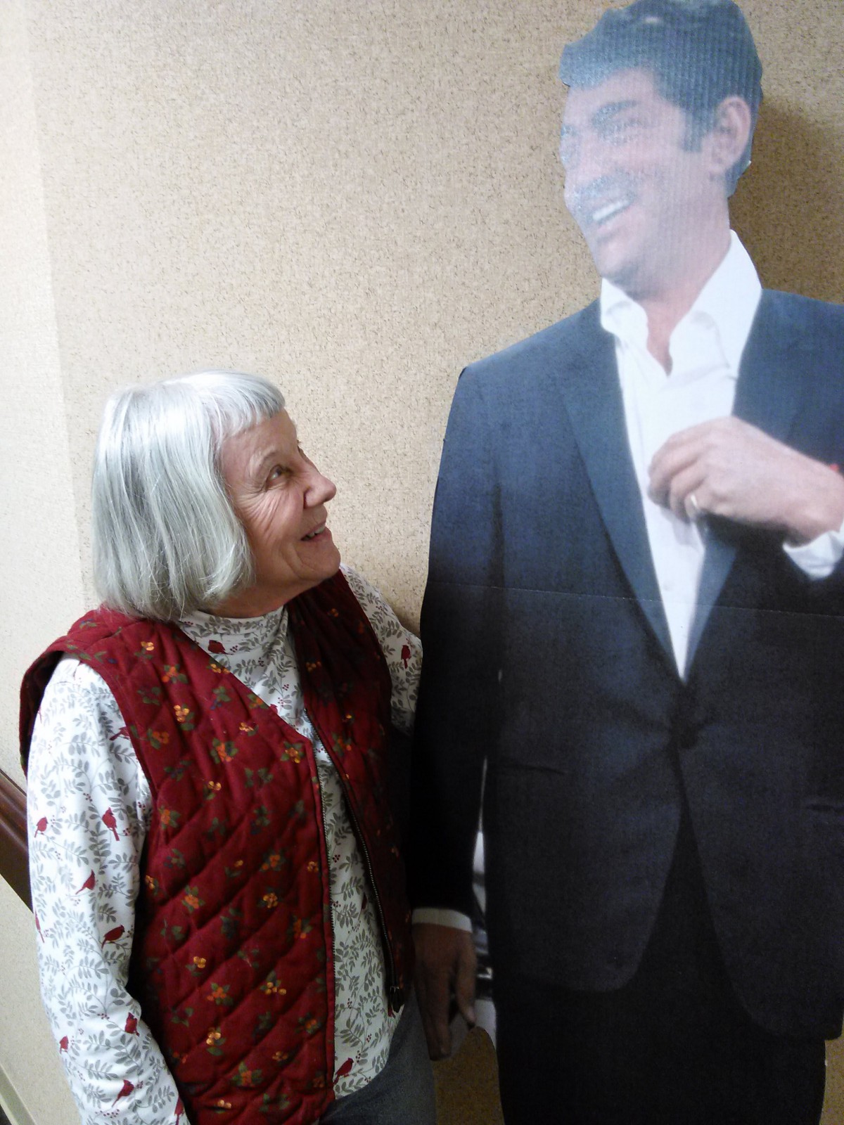 An elderly woman smiling at a cardboard cutout of a man in a suit.