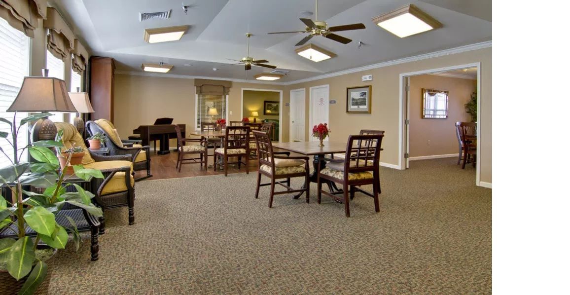 A spacious and well-lit room with several tables and chairs, ceiling fans, and a piano in the corner.