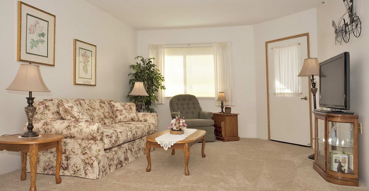 A cozy living room with a floral sofa, armchair, coffee table, and window.