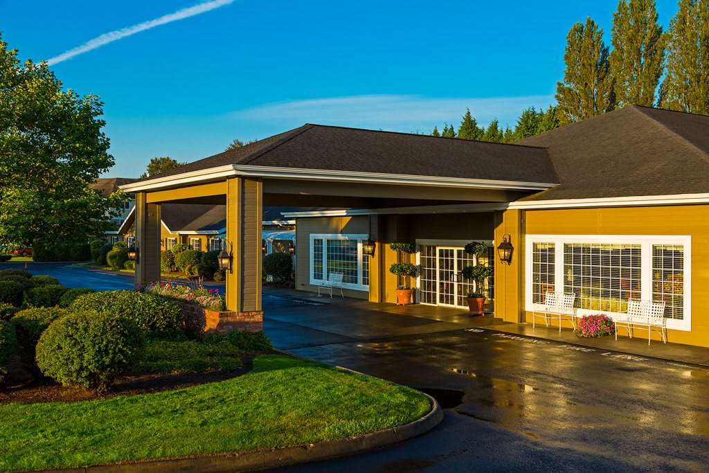 A well-lit building entrance surrounded by greenery under a clear blue sky.