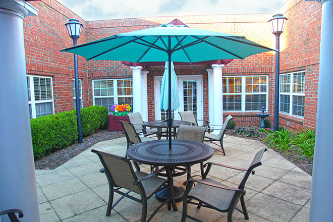 A cozy outdoor patio setup with a large umbrella and seating arrangement in front of a brick building.