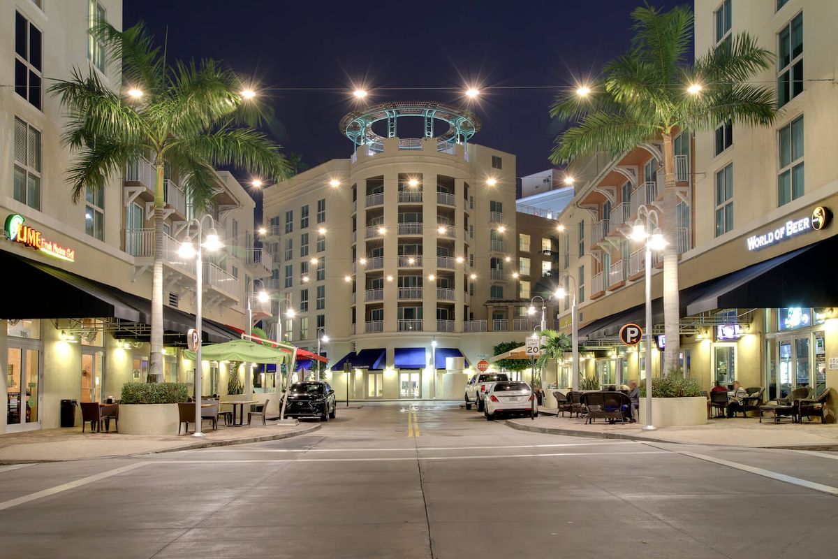 A beautifully lit urban street scene with palm trees and a prominent building at night.