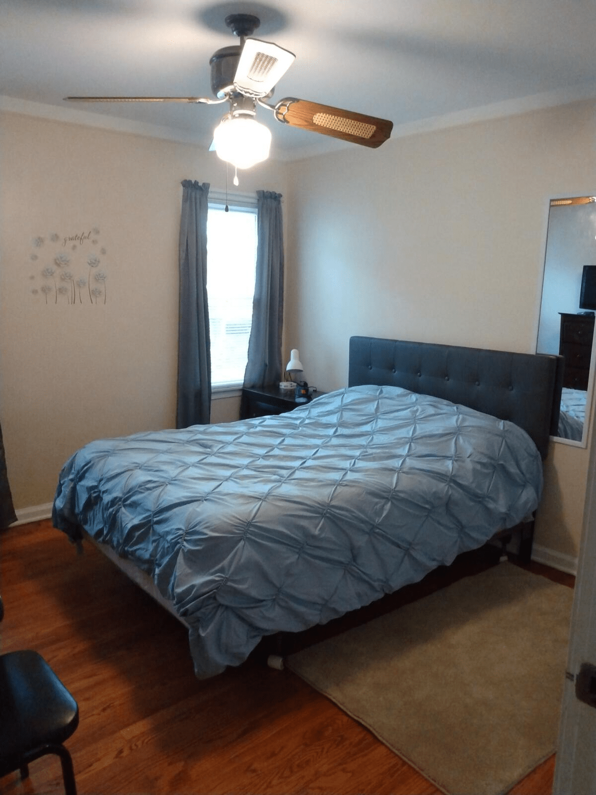 A cozy bedroom with a neatly made bed, curtains, and a ceiling fan.