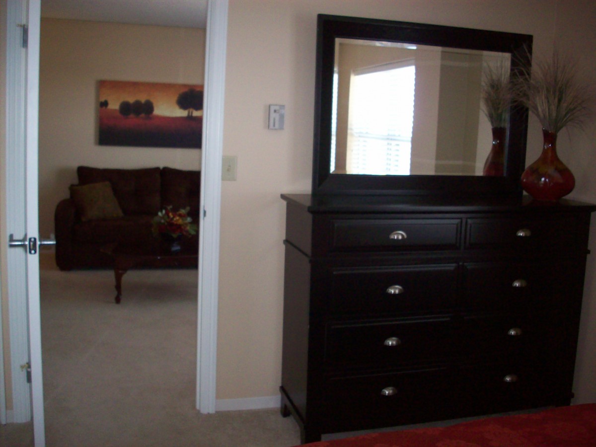 A bedroom featuring a dark dresser with a mirror, and an adjacent room visible through an open door.