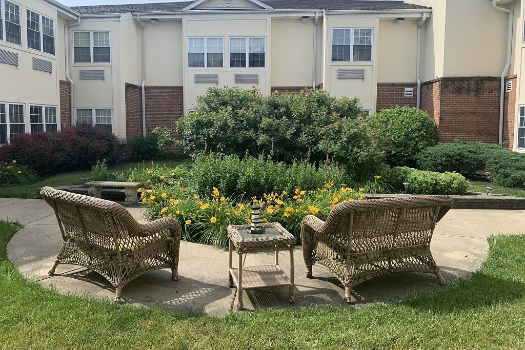A cozy outdoor patio with wicker chairs overlooking a lush garden in front of a residential building.