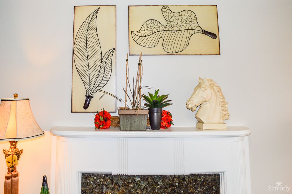 A well-decorated mantel featuring modern leaf artwork, a small plant arrangement, and a horse head sculpture.