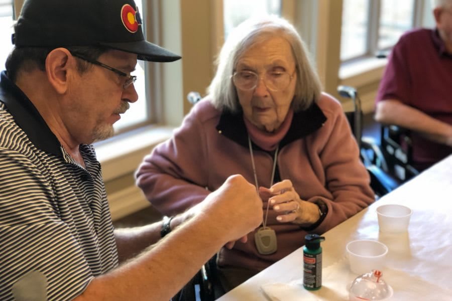 An elderly woman in a wheelchair is interacting with a man wearing a hat indoors.