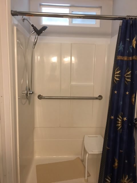 A bathroom shower with a dark blue curtain and a grab bar installed.