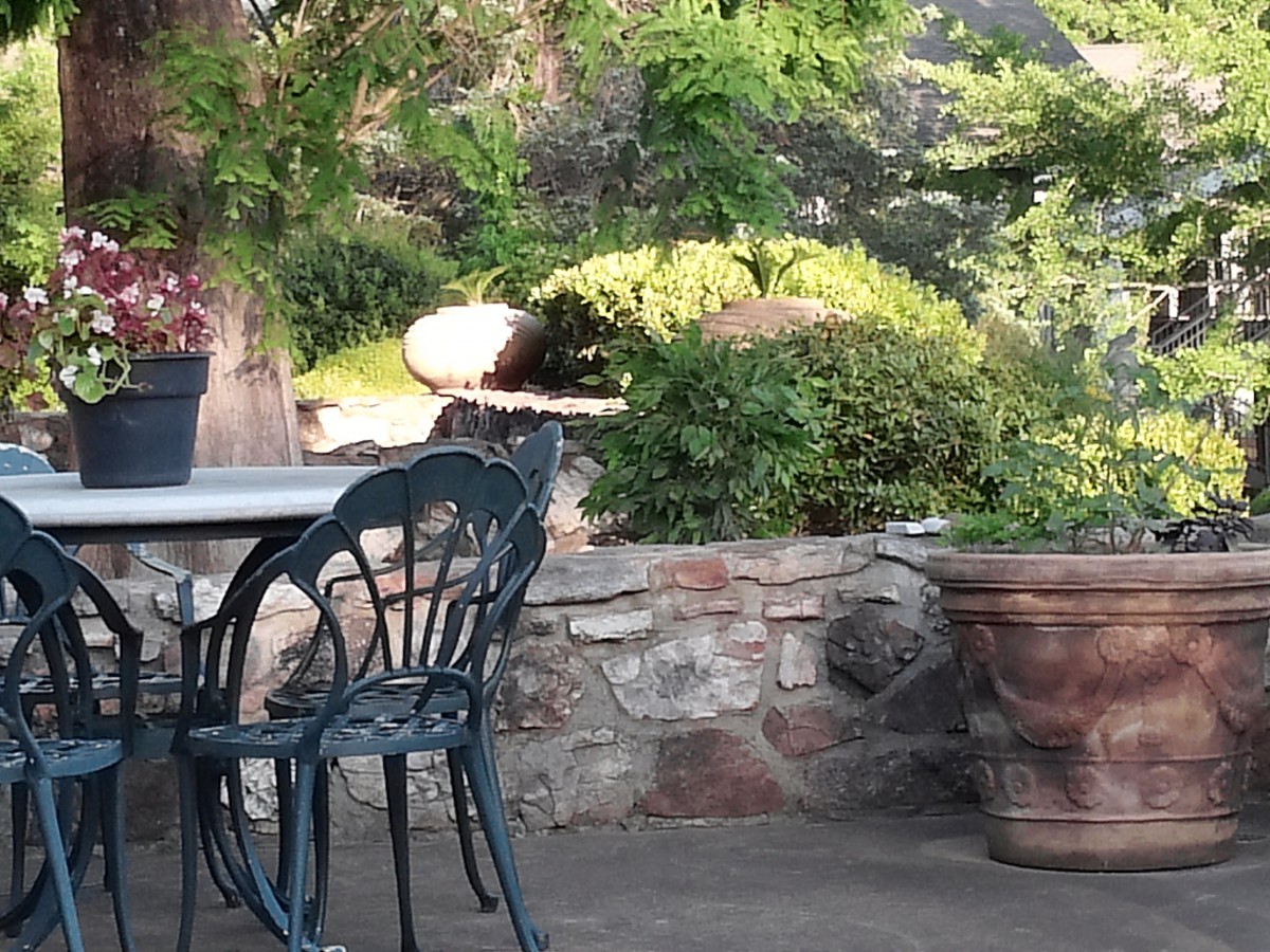 A tranquil patio area with outdoor seating surrounded by lush greenery and a stone wall.