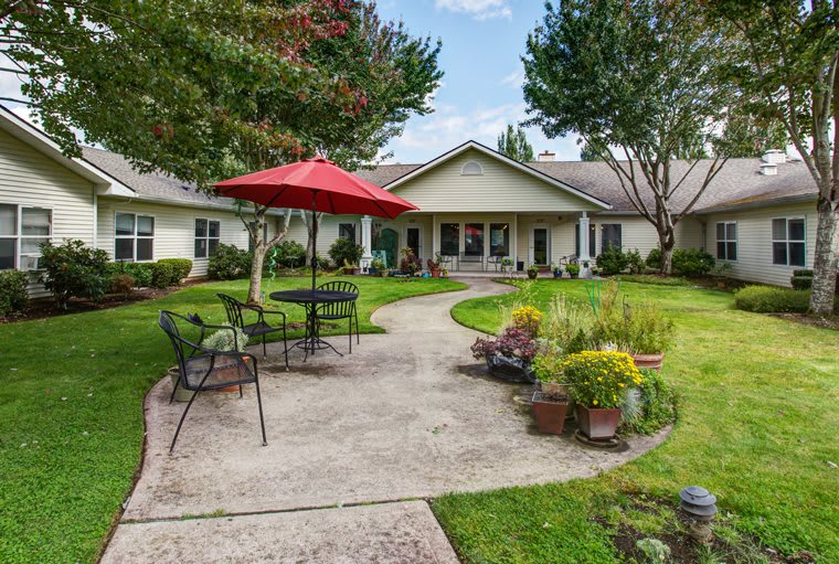 A charming house with a well-maintained garden and patio area, featuring outdoor furniture and a red umbrella.