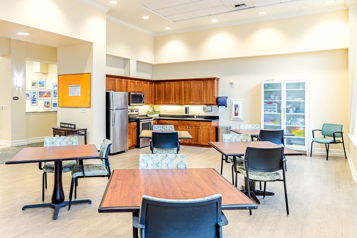 A modern communal kitchen and dining area with wooden tables, chairs, and stainless steel appliances.