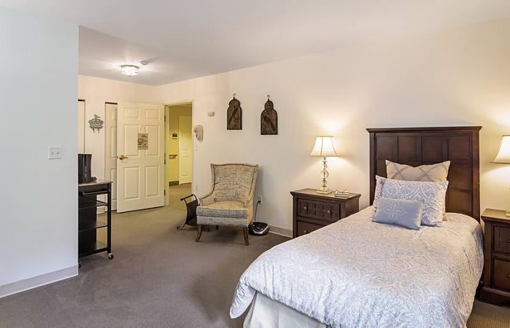 A cozy and well-furnished bedroom with a bed, chair, and lamp.