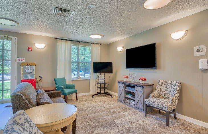 A cozy living room with comfortable seating, two televisions, and a large window allowing natural light to fill the space.