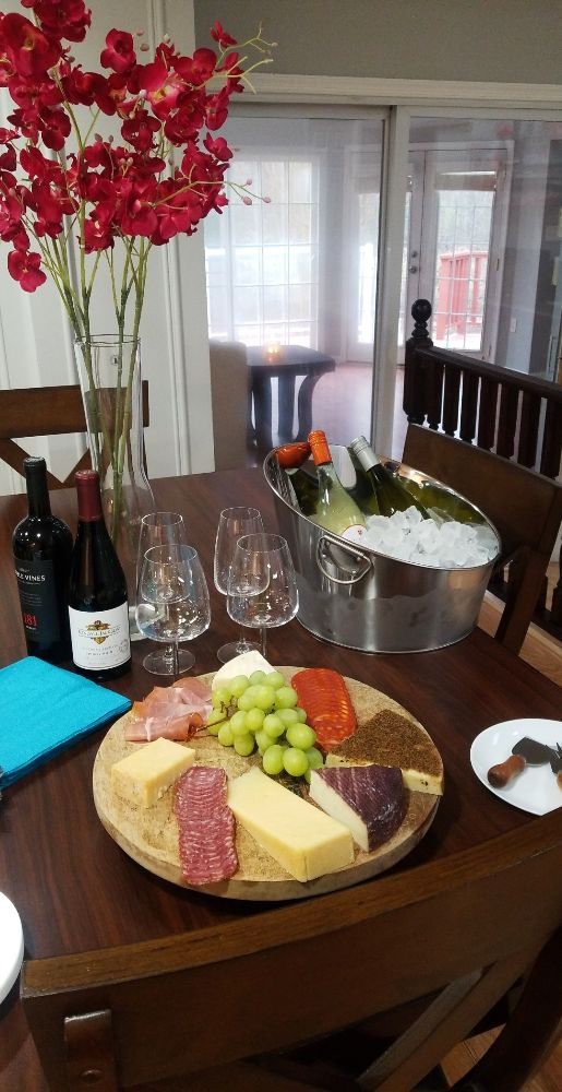 A table set with a cheese and charcuterie board, accompanied by wine bottles and glasses, with an ice bucket chilling more beverages.
